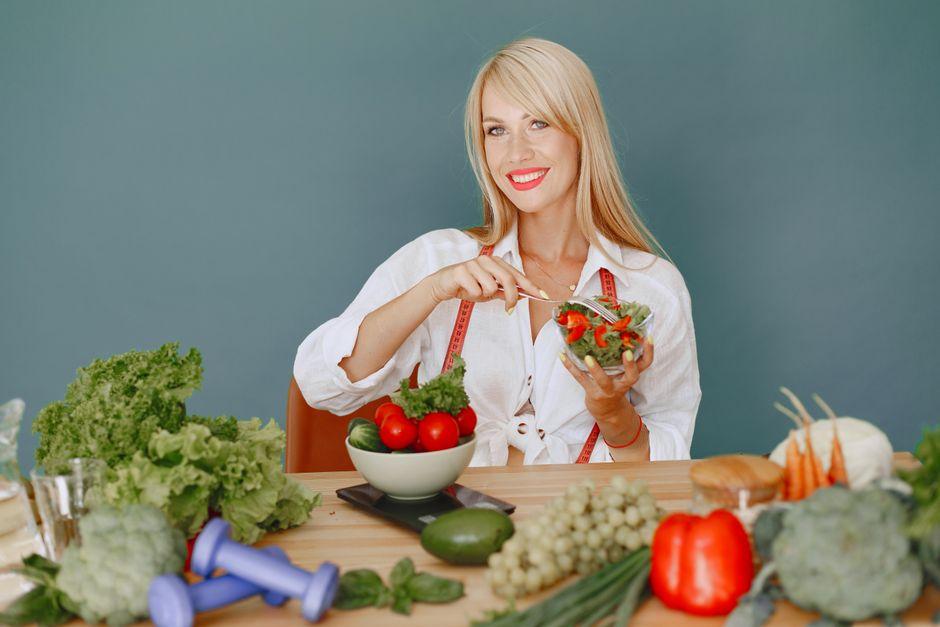Woman Holding a Bowl with Salad While Sitting Behind a Table Full of Vegetables