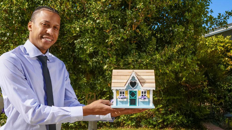 Man in Dress Shirt Holding a Miniature Wooden House
